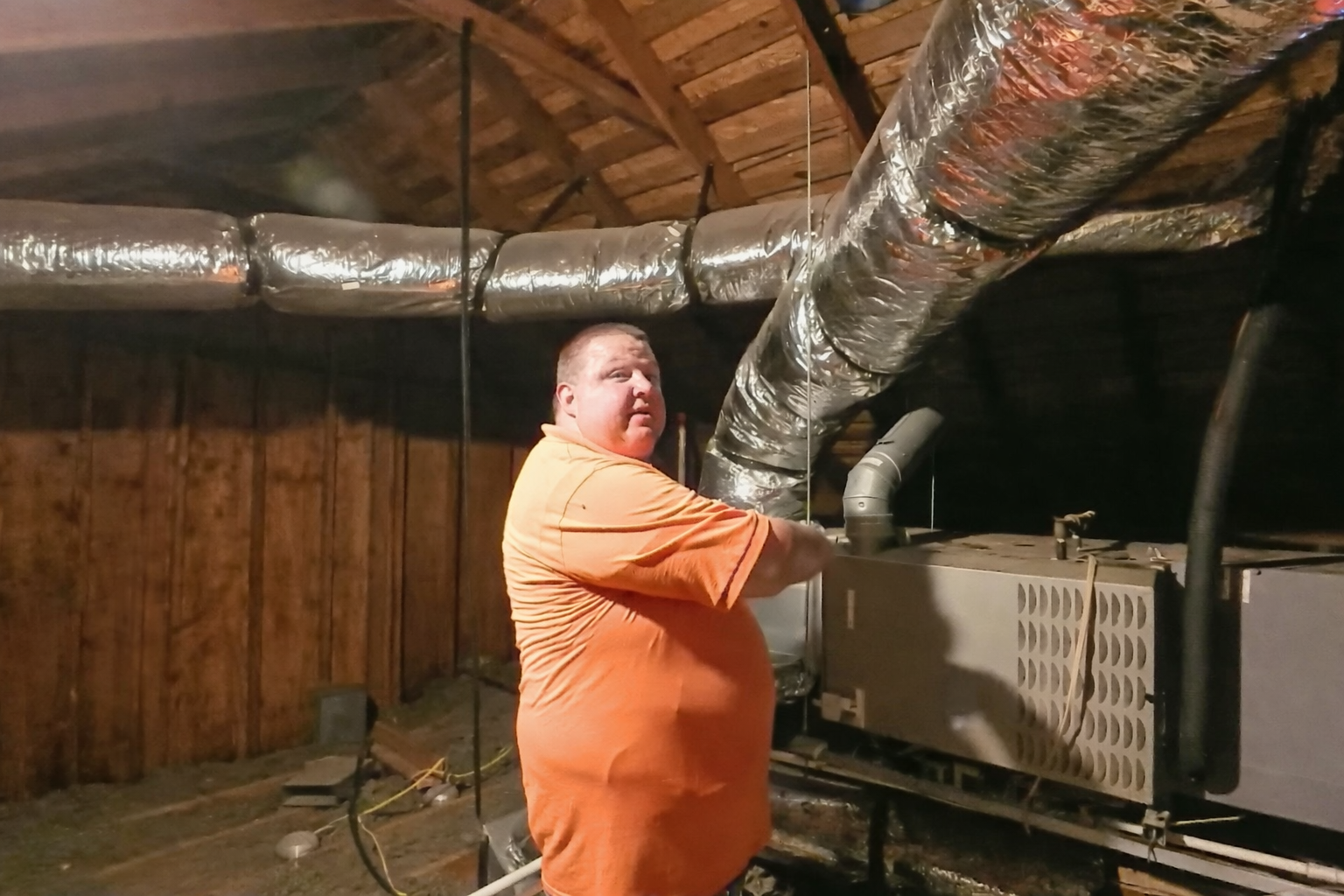 HVAC technician showing ductwork and air distribution above a residential system in an attic